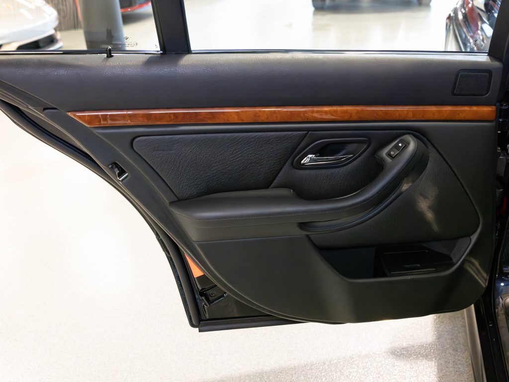 Car interior showing an open rear passenger door with black leather, wooden trim, and a control panel for the window. - Monarch Showroom