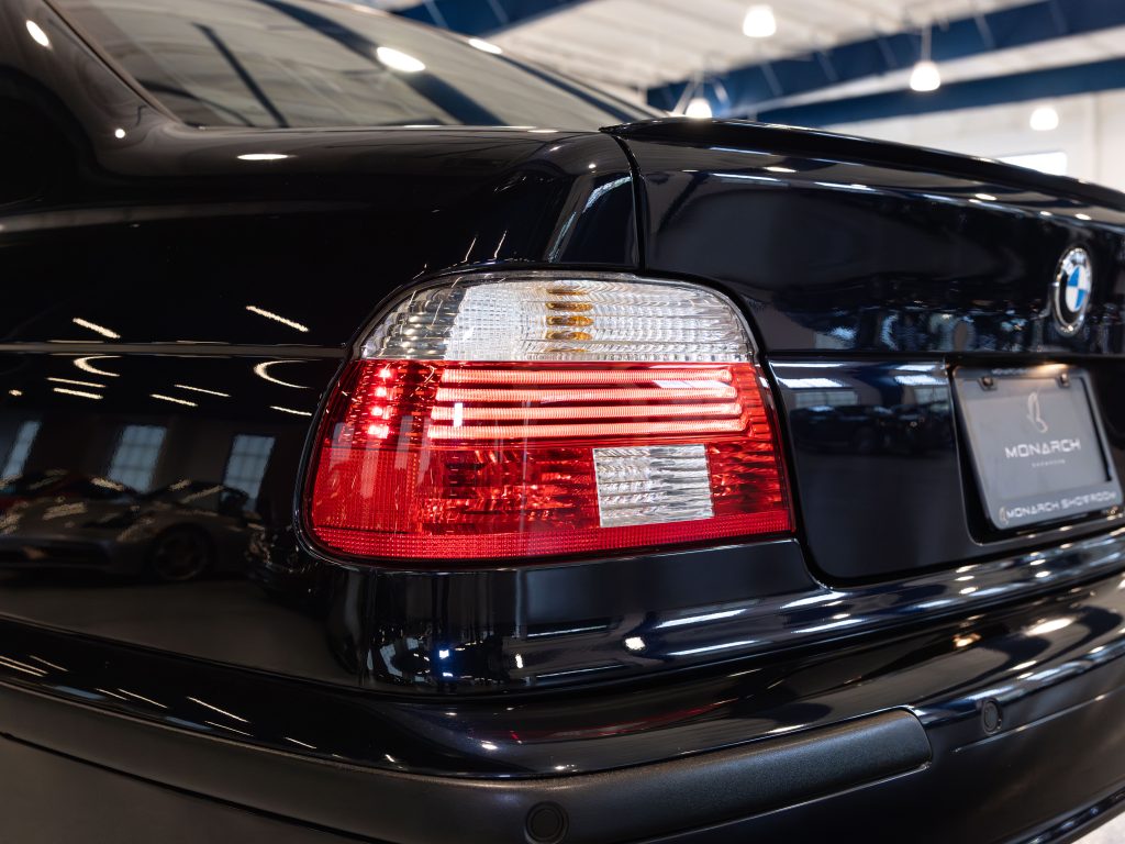 Close-up of the rear of a black BMW car, showcasing the tail lights and part of the trunk, with a license plate and showroom in the background. - Monarch Showroom