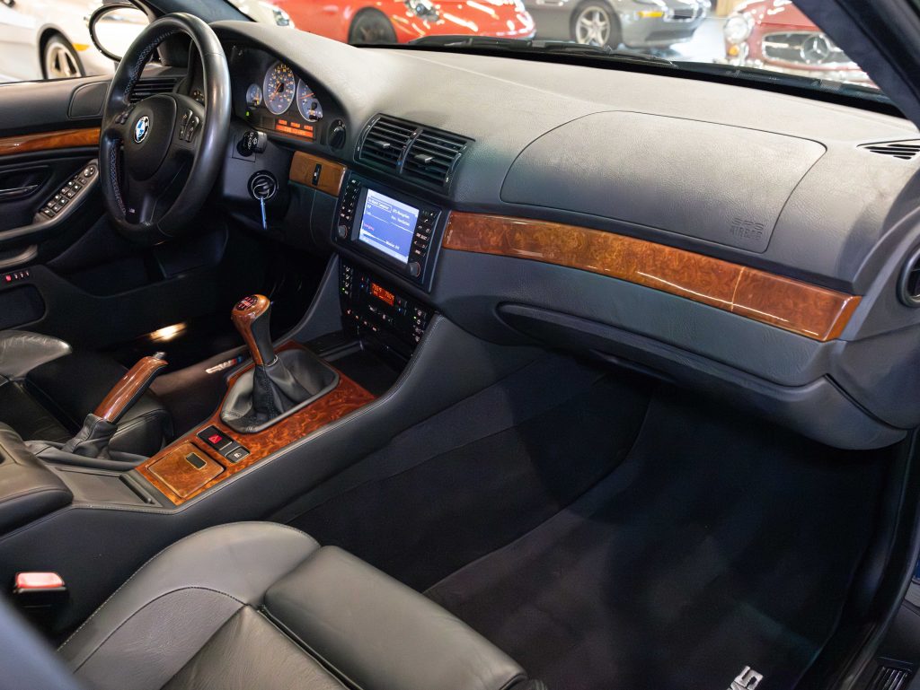 Interior of a car showcasing a manual transmission, wood trim, leather seats, and a digital display on the dashboard. - Monarch Showroom