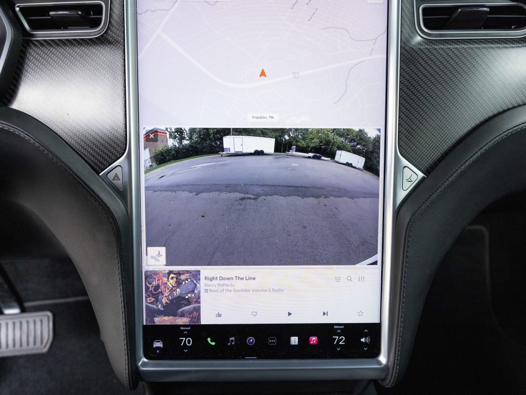 Car dashboard touchscreen displays a rearview camera feed, music player interface, and navigation map. Temperature controls are set to 70 and 72 degrees. - Monarch Showroom